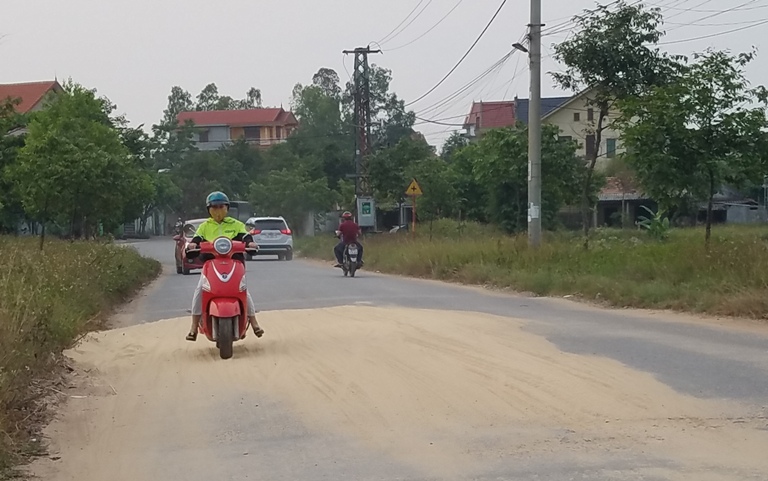 Một người đi xe máy phải rà hai chân xuống để giữ thăng bằng khi đi qua đoạn đường bị cát tràn xuống.