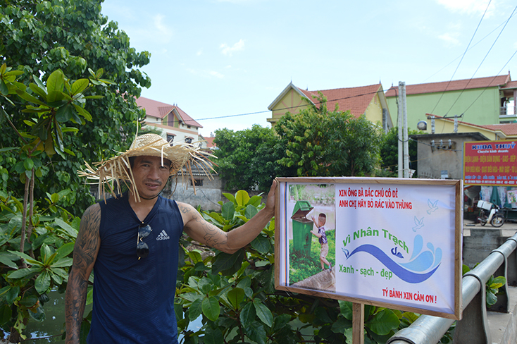 Anh Đinh Tý bên tấm biển tuyên truyền, vận động bà con cùng chung tay vì một Nhân Trạch xanh, sạch, đẹp. (Ảnh: P.P) 