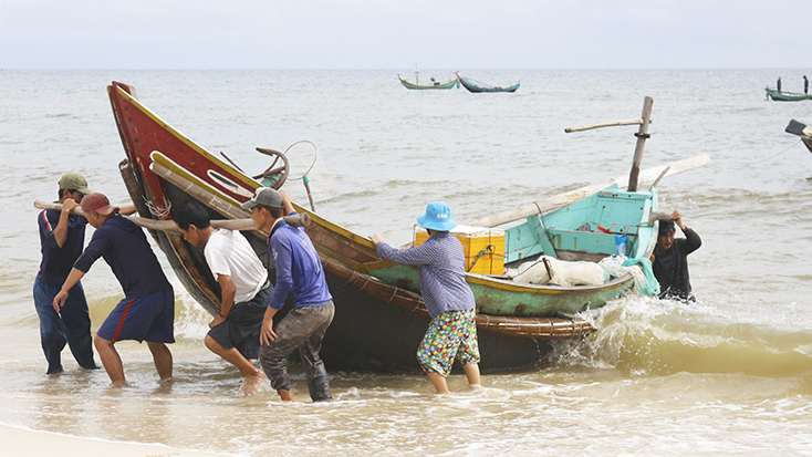 Ngư dân đẩy thuyển lên bờ, sau chuyến biển đêm.
