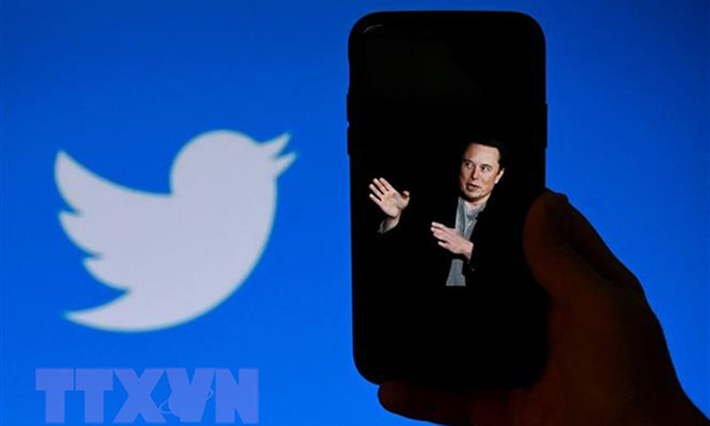 Chân dung tỷ phú Elon Musk trên màn hình điện thoại và biểu tượng Twitter (phía sau). (Ảnh: AFP/TTXVN)