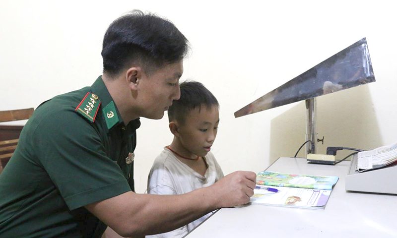 Với nghĩa cử hướng về đồng bào khu vực biên giới, BĐBP đã nhận các cháu học sinh dân tộc thiểu số mồ côi, có hoàn cảnh khó khăn làm con nuôi, đưa về đơn vị chăm sóc. Trong ảnh: Cán bộ Đồn Biên phòng Nậm Kè, BĐBP Điện Biên hướng dẫn con nuôi của đơn vị học bài. Ảnh: Bích Nguyên