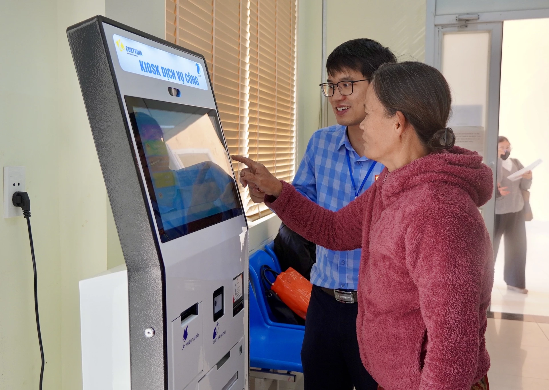 Cán bộ Trung tâm Phục vụ hành chính công phường Đồng Thuận hỗ trợ người dân lấy số tự động khi đến giao dịch tại trung tâm - Ảnh: Đ.V