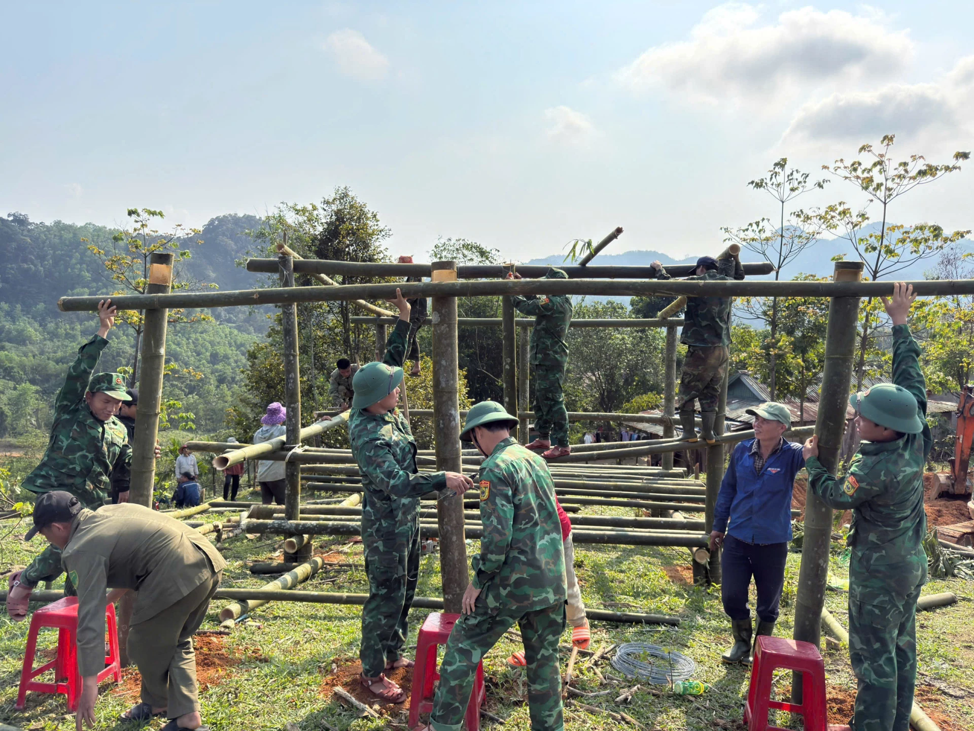 Cán bộ, chiến sĩ Đồn Biên phòng Ba Nang cùng người dân địa phương khẩn trương dựng khung nhà bằng tre giúp gia đình anh Hồ Văn Hồi-Ảnh: K.S