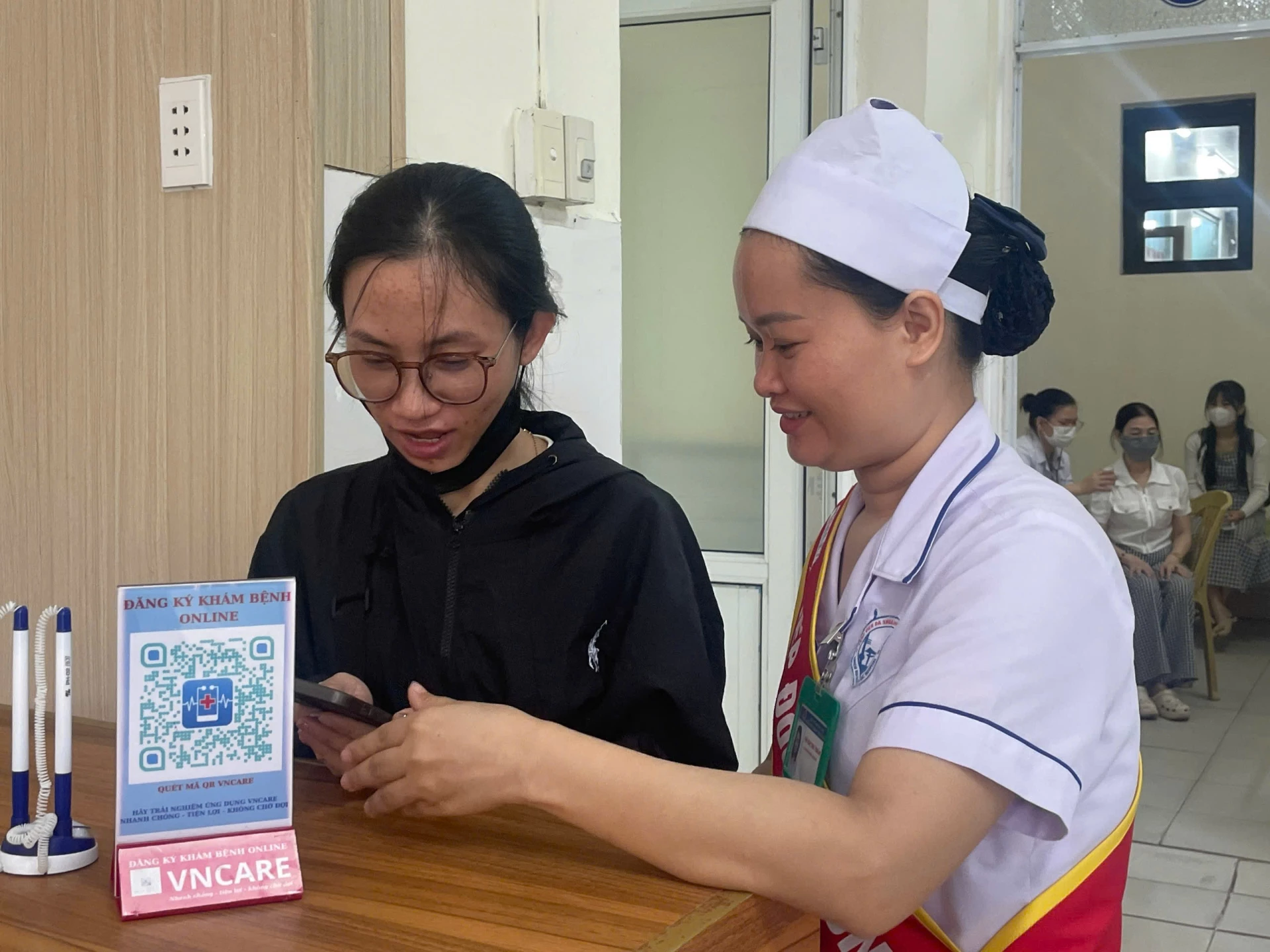Nhân viên y tế hướng dẫn người dân đăng kí khám bệnh online - Ảnh: H.N