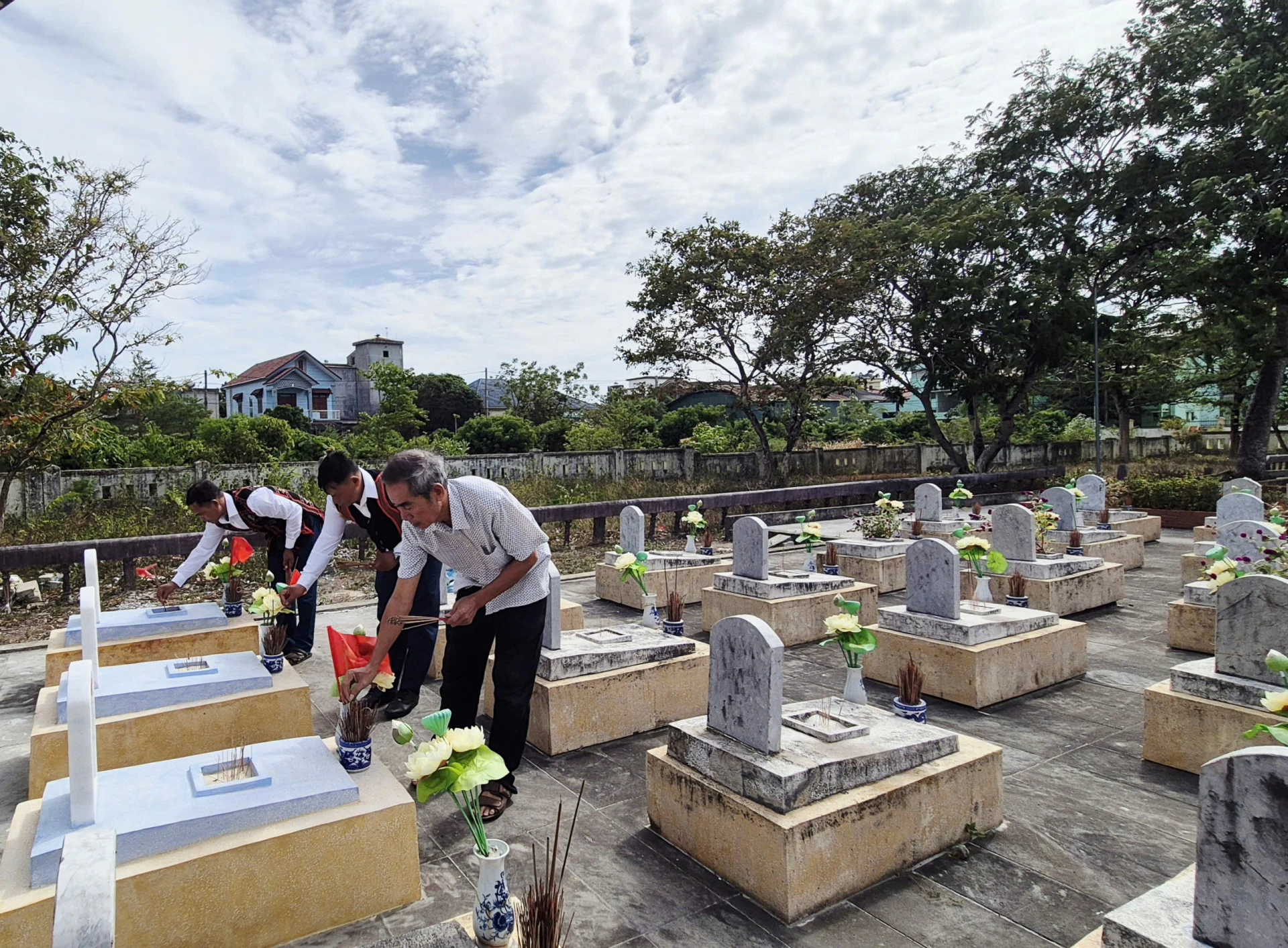 Ông Nguyễn Ngọc Tân (bên phải ngoài cùng) và anh Hồ Văn Phương (bên trái ngoài cùng) thắp hương tại các phần mộ liệt sĩ vừa được quy tập về nghĩa trang-Ảnh: K.S