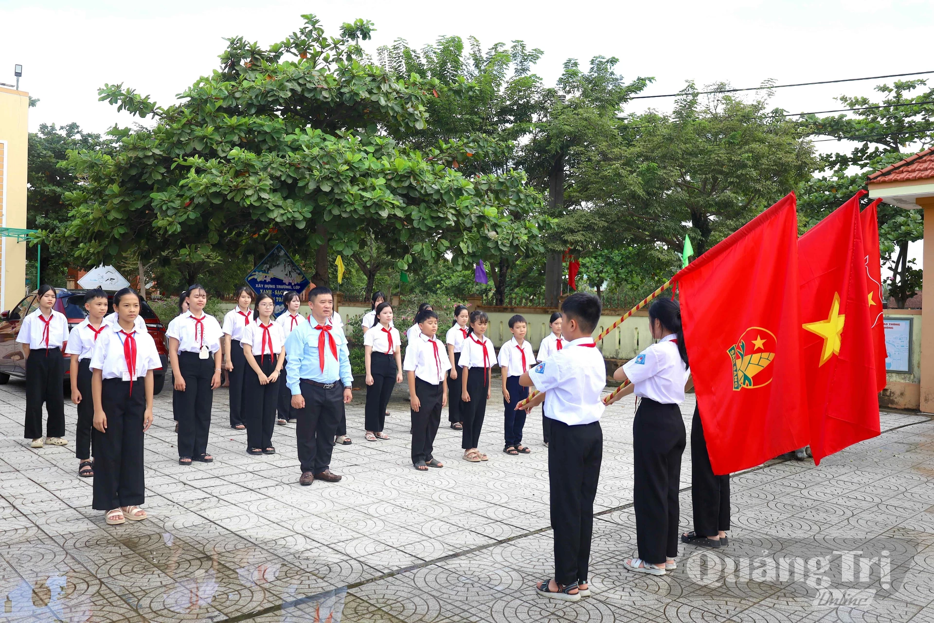 Thầy giáo Hồ Văn Hợi hướng dẫn đội viên luyện tập nghi thức Đội tại sân trường - Ảnh: Q.N