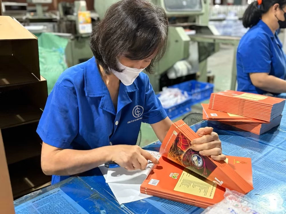 Công nhân thực hiện công đoạn dán tem cho sách giáo khoa. (Ảnh: Phạm Mai/Vietnam+)