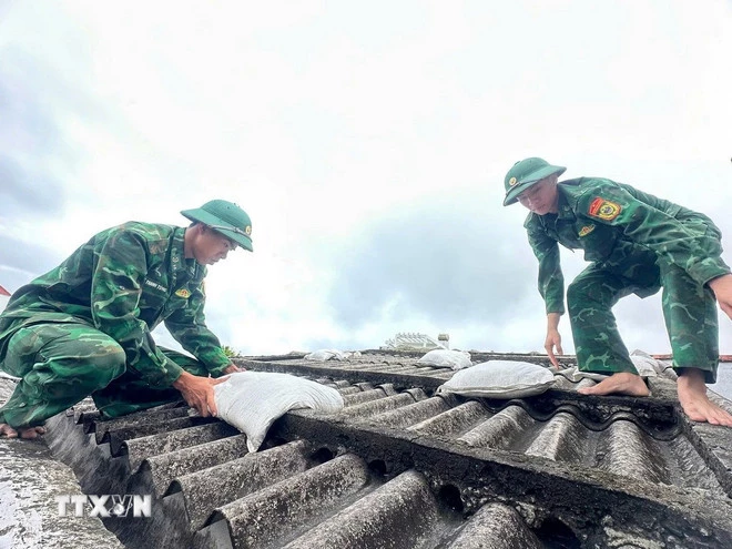 Các chiến sĩ giúp người dân đưa bao cát lên mái nhà để tránh tốc mái tôn khi gió bão. (Ảnh: TTXVN phát)