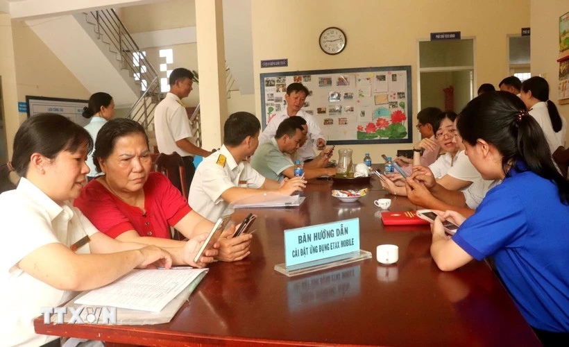 Cán bộ ngành thuế hướng dẫn người dân cài đặt ứng dụng eTax Mobile. (Ảnh: Thu Hiền/TTXVN)